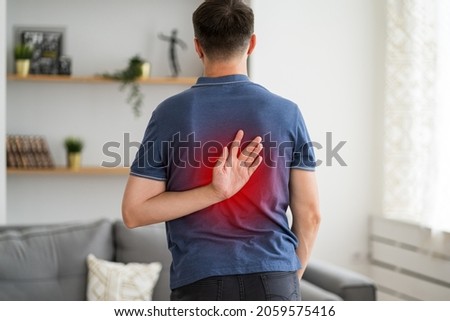 Pain between the shoulder blades, man suffering from backache at home, painful area highlighted in red Royalty-Free Stock Photo #2059575416