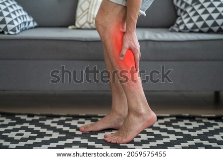 The man's calf muscle cramped, massage of male leg at home, painful area highlighted in red Royalty-Free Stock Photo #2059575455