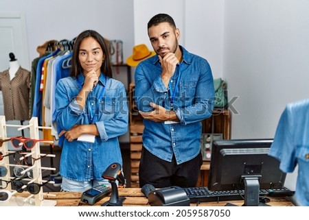 Young interracial people working at retail boutique looking confident at the camera with smile with crossed arms and hand raised on chin. thinking positive. 