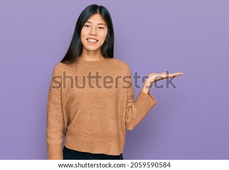 Beautiful young asian woman wearing casual winter sweater smiling cheerful presenting and pointing with palm of hand looking at the camera. 