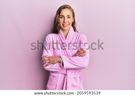 Young blonde woman wearing bathrobe happy face smiling with crossed arms looking at the camera. positive person. 