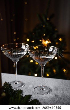Two glasses of champagne with lights in the background. Nearby there are decorations and a wreath of greenery. Shallow depth of field for atmospheric photography. Christmas together on the background 