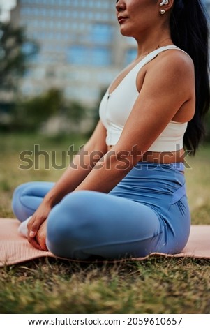 Close up of unrecognizable woman sitting on yoga mat with crossed legs and meditating in the park