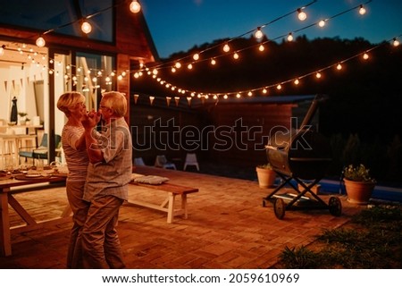 Beautiful senior couple dancing together in their backyard decorated with lamps