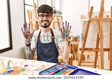 Hispanic man with beard at art studio showing and pointing up with fingers number ten while smiling confident and happy. 