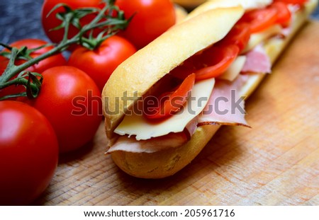 delicious baguette sandwiches filled with thinly sliced ham or salami and fresh green lettuce or basil and tomatoes arranged in an wooden table
