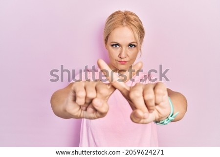 Young blonde woman wearing casual pink t shirt rejection expression crossing fingers doing negative sign 