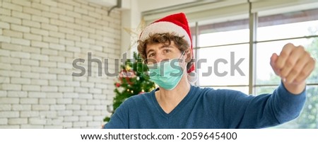 Single male wearing facial mask and santa hat in home decoration of christmas party in Covid-19 situation concept