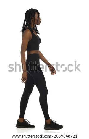 Walking black woman in sports clothes and snekares. Side view. Full length studio shot isolated on white.