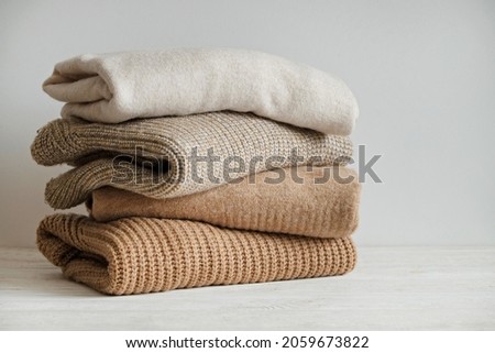 Bunch of knitted warm pastel color sweaters with different knitting patterns stacked in messy pile on white wooden table, white wall background. Fall winter season knitwear. Close up, copy space. Royalty-Free Stock Photo #2059673822