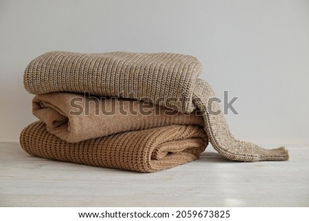 Bunch of knitted warm pastel color sweaters with different knitting patterns stacked in messy pile on white wooden table, white wall background. Fall winter season knitwear. Close up, copy space. Royalty-Free Stock Photo #2059673825