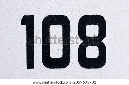 A number one hundred and eight - 108. Black lettering on a white stucco wall