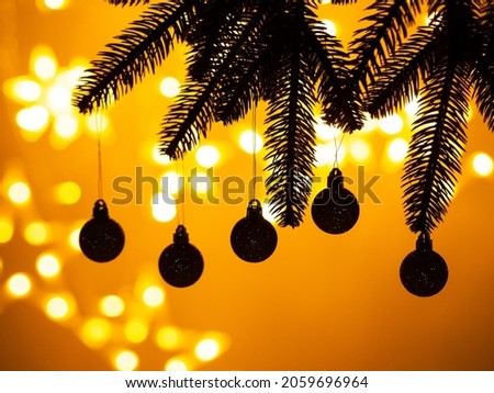 Christmas tree branches silhouette with five new year balls on golden yellow background with bokeh lights. Winter holiday concept card.
