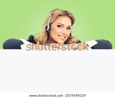 Call center. Customer support service female phone operator or sales agent in headset, grey confident suit standing behind mock up signboard with copy space area, isolated over light green color back.