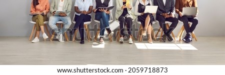 Diverse people in smart casual clothes holding paper documents, CVs, resumes, laptops and cellphones waiting in line for job interviews or business appointments in recruitment agency, legs low section Royalty-Free Stock Photo #2059718873