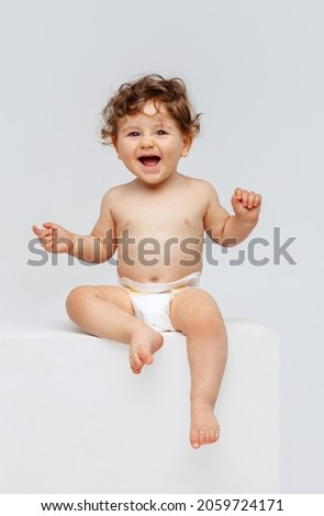 Smiling happy child. Portrait of little toddler boy, baby in diaper joyfully sitting and laughing isolated on white studio background. Concept of childhood, motherhood, life, birth. Copy space for ad Royalty-Free Stock Photo #2059724171
