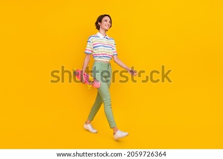 Full size profile side photo of young girl happy positive smile walk longboard hobby isolated over yellow color background