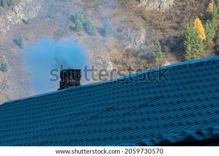 Gray smoke coming from the chimney of a residential building. Brick chimney on the roof of the house. Royalty-Free Stock Photo #2059730570