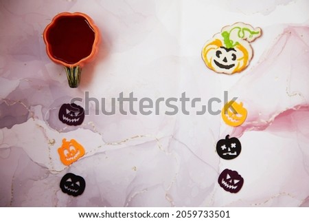 Homemade pumpkin cookie and cup of tea in shape of pumpkin. Halloween felted decorations with copy space on fluid art background. Autumn holidays concept. High quality photo. 