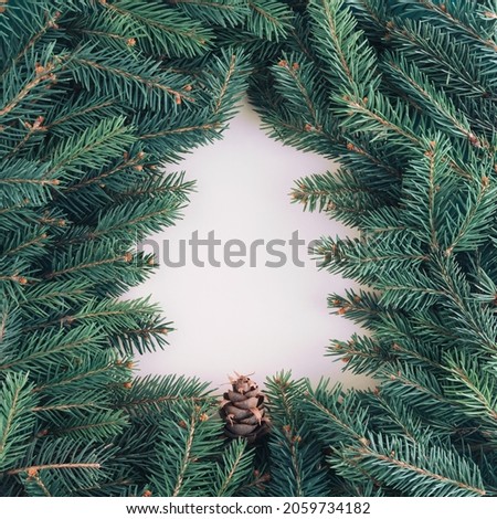 2022 Minimal New Year background with beige Christmas tree shaped negative space and green fir branches around them. Natural winter holiday pattern. Greeting or invitation card idea. Minimal flat lay.