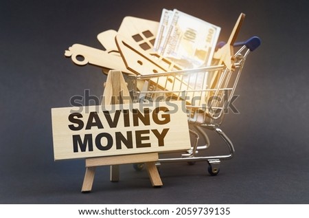 Business and finance concept. On a black background, there is a shopping cart with purchases, next to an easel and a sign with the inscription - SAVING MONEY