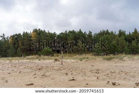 Haapse Estonia - October 14 2021: Sandy beach in front of pine forest. Log louse hidden behind trees. Wooden simple fence posts connected with rope. Cloudy autumn day.