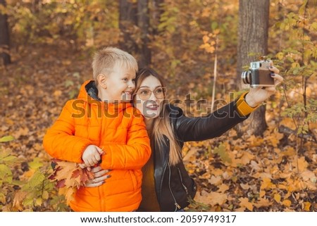 Son and mother are taking selfie on camera in autumn park. Single parent, leisure and fall season concept.