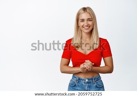 Image of young pleasant woman asking what you need, assistant looking polite and friendly at camera, standing over white background