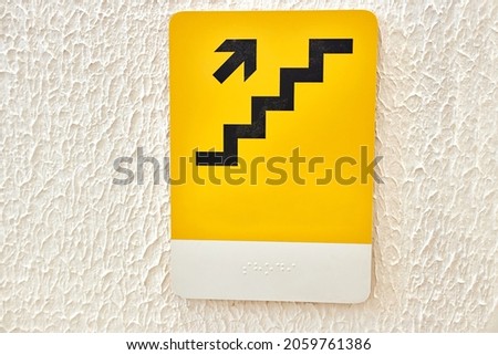 Yellow sign with step up symbols and pointing arrow and Braille inscription.