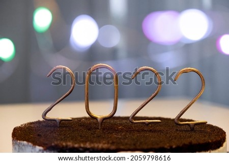Golden candles with 2022 number on top of chocolate cake with bokeh lights on background. Merry Christmas and Happy New Year celebration atmosphere.