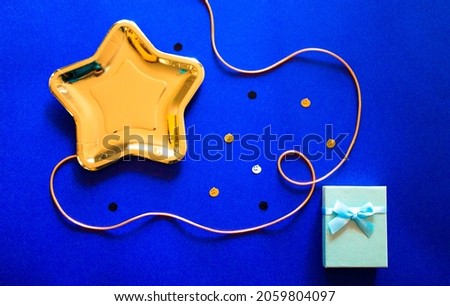 Halloween table. A gold star shaped plate, gift box, festive decor on blue background. Oct. 31. Stylish party ware. Jack o lantern pumpkin shaped confetti flatly Thanksgiving dinner creative wallpaper