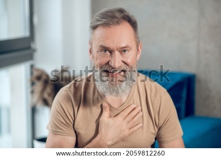 A waist up picture of a a bearded man putting hand on his heart