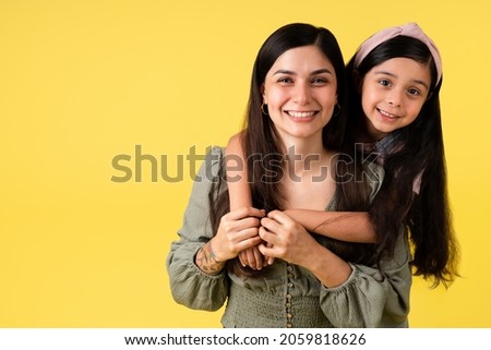 Portrait of a cute little girl hugging her attractive latin mom in front of a yellow background