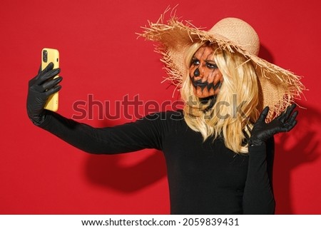 Young woman with Halloween makeup mask wears straw hat black scarecrow costume doing selfie shot on mobile cell phone isolated on plain red background studio portrait Celebration holiday party concept