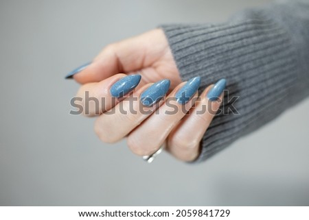 Woman's beautiful hand with long nails and light blue manicure with bottles of nail polish	