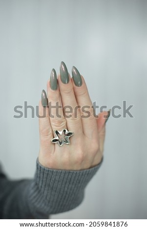 Female hand with long nails and gray green manicure with bottles of nail polish