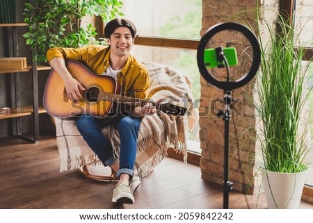 Photo of blogger musician guy sit armchair play guitar make performance live video wear yellow shirt home indoors