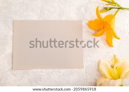 Gray paper business card mockup with orange day-lily flower on gray concrete background. Blank, top view, copy space, still life. spring concept.