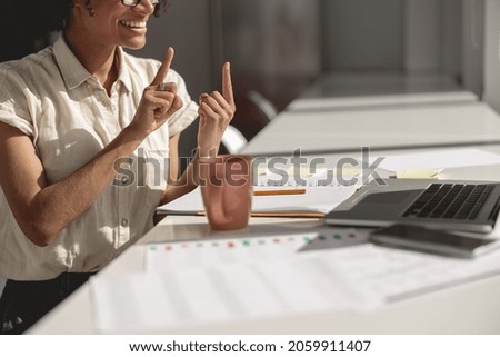 Smiling young lady learning and communicating in sign language online while sitting at workplace Royalty-Free Stock Photo #2059911407