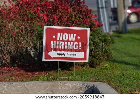 Outdoor lawn sign now hiring apply inside with direction arrow, selective focus. Great resignation, employment, understaffed business, work strikes, absent workers due to covid labor shortage concept.