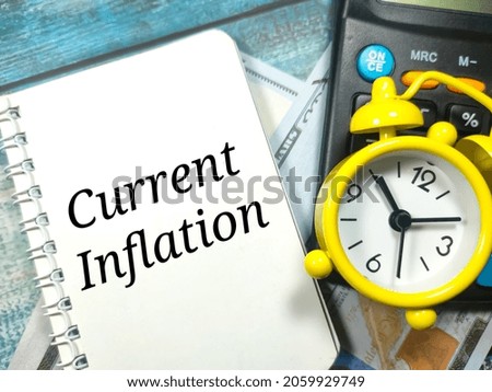 Selective focus.Text Current Inflation written on notebook with clock,calculator and banknotes on blue wooden background. Business concept.