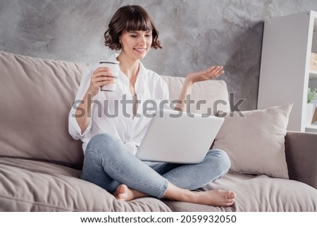 Photo portrait woman wearing white shirt using computer drinking coffee at home on couch talking on web camera Royalty-Free Stock Photo #2059932050