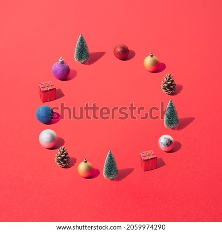 Arranged green snow Christmas tree with colorful baubles in circle shape on red pastel background.