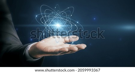Close up of businessman hand holding abstract glowing atom hologram on dark background. Science and connection concept
