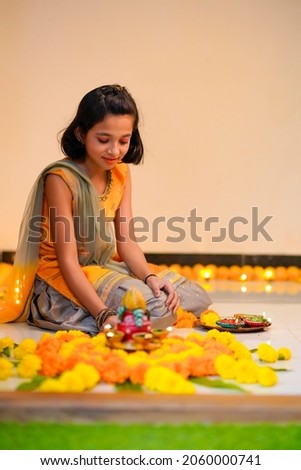 Cute indian little girl making decoration with flower and oil lamp for diwali festival at home