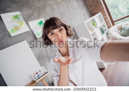 Photo portrait young girl wearing casual shirt taking selfie sending air kiss near blank canvas