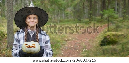 a girl in a witch costume holding a pumpkin lantern, halloween concept, a girl in a plaid shirt and a witch felt hat playing with a jack lantern in the forest copy space banner