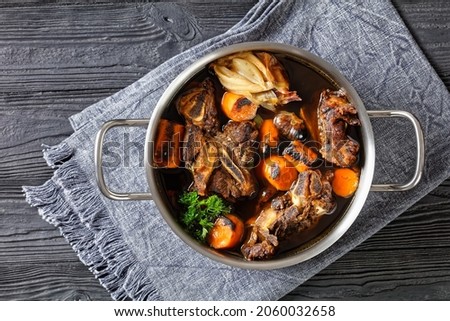 beef broth of beef meat on bones slow cooked with charred vegetables: carrot, onion, garlic, and spices served in a pot on a wooden table, top view, flat lay, free space