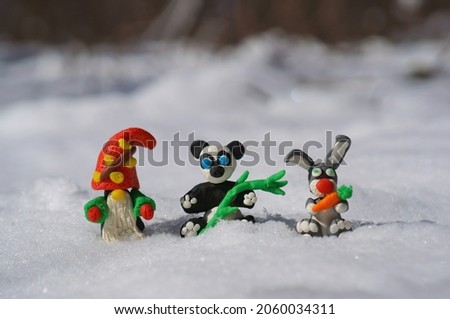A dwarf, a panda and a rabbit made of plasticine on a background of snow.