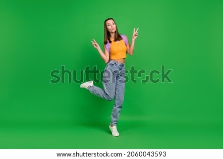 Full length photo of young cheerful funky woman make v-signs wear backpack isolated on green color background